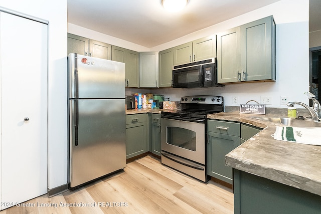 kitchen featuring sink, light hardwood / wood-style flooring, green cabinetry, and appliances with stainless steel finishes