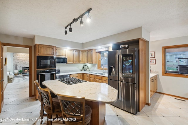 kitchen with a textured ceiling, sink, black appliances, a fireplace, and a kitchen island