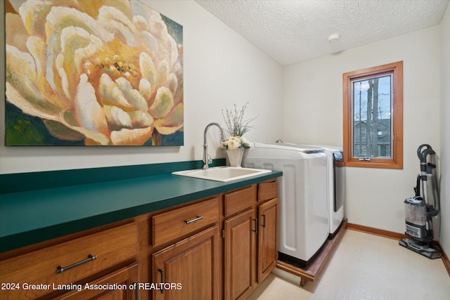 clothes washing area with cabinets, sink, washer and dryer, and a textured ceiling