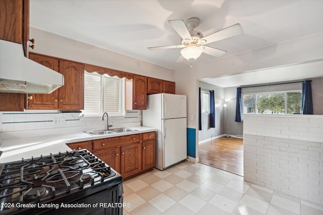 kitchen featuring black gas range, sink, light hardwood / wood-style flooring, ceiling fan, and white fridge