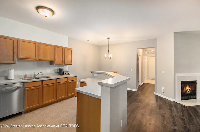 kitchen with sink, a premium fireplace, stainless steel dishwasher, pendant lighting, and light wood-type flooring