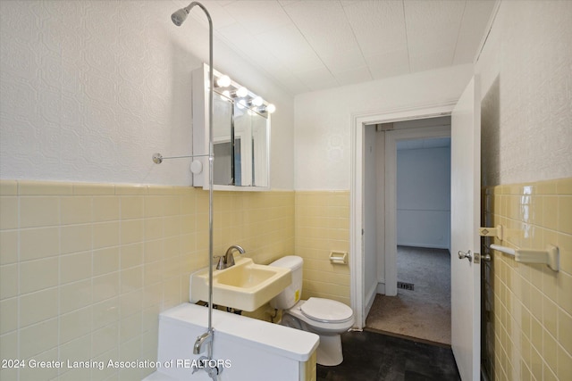 bathroom with toilet, sink, and tile walls