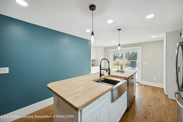 kitchen with dishwasher, a center island with sink, white cabinets, decorative light fixtures, and light hardwood / wood-style floors