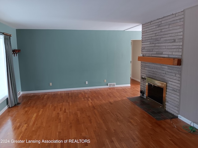 unfurnished living room featuring wood-type flooring and a brick fireplace