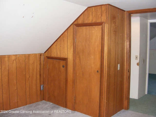 additional living space with wood walls, light carpet, and vaulted ceiling