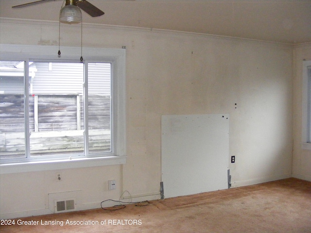 empty room featuring ornamental molding, light colored carpet, ceiling fan, and a healthy amount of sunlight