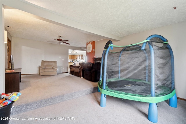 recreation room featuring carpet flooring, ceiling fan, and a textured ceiling