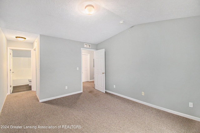 unfurnished bedroom with carpet flooring, a textured ceiling, ensuite bath, and lofted ceiling