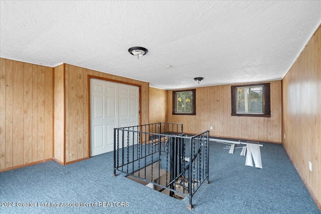 playroom with wood walls, dark carpet, and a textured ceiling