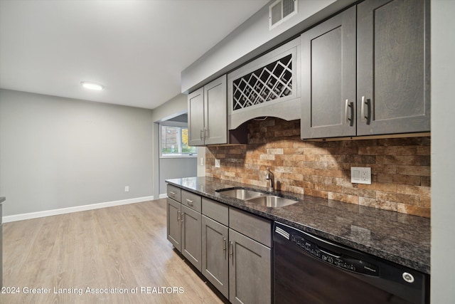 kitchen featuring dishwasher, sink, dark stone countertops, decorative backsplash, and light wood-type flooring