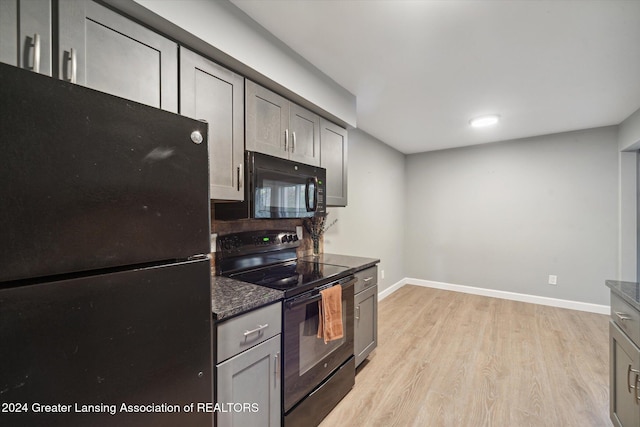 kitchen with black appliances, gray cabinets, dark stone countertops, and light wood-type flooring