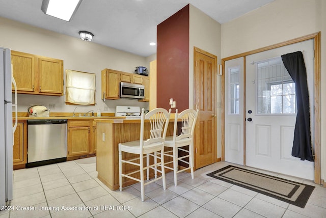 kitchen with a kitchen breakfast bar, kitchen peninsula, light tile patterned floors, and stainless steel appliances