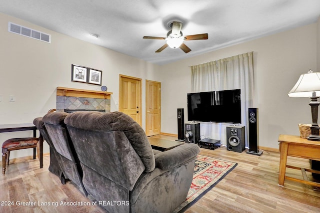 living room with a tile fireplace, ceiling fan, and light hardwood / wood-style flooring