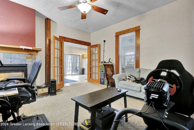 home office with carpet flooring, ceiling fan, french doors, a textured ceiling, and a tiled fireplace