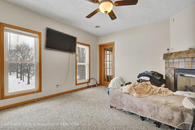 carpeted bedroom featuring a textured ceiling, ceiling fan, and a tiled fireplace