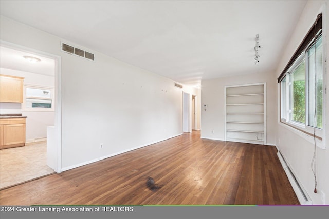 unfurnished room featuring built in shelves, dark wood-type flooring, and a baseboard radiator