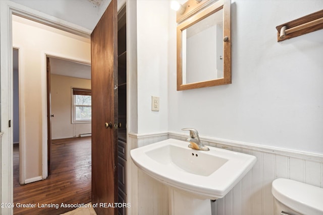 bathroom featuring hardwood / wood-style floors, wood walls, toilet, and sink