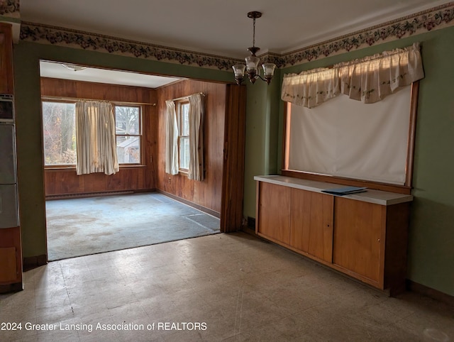 unfurnished dining area with wooden walls, light carpet, a baseboard radiator, and an inviting chandelier