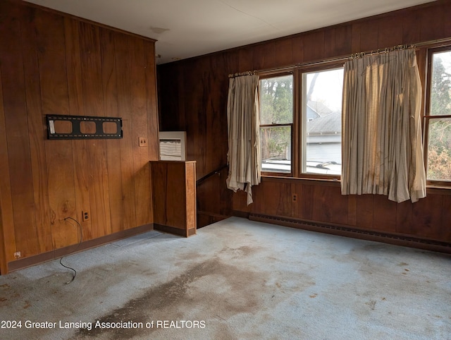 empty room featuring wood walls, light colored carpet, and a baseboard radiator