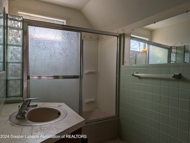 bathroom with vanity, combined bath / shower with glass door, tile walls, and vaulted ceiling