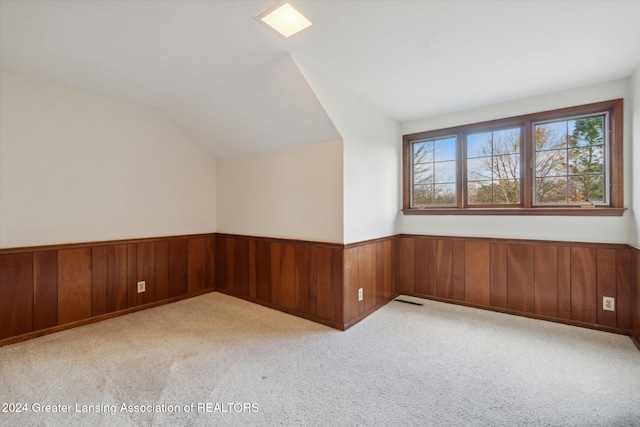 empty room with light carpet, wooden walls, and lofted ceiling