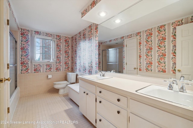 full bathroom featuring tile patterned floors, combined bath / shower with glass door, toilet, vanity, and tile walls