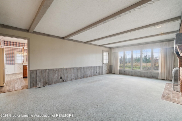 carpeted empty room with beamed ceiling, a textured ceiling, and wood walls