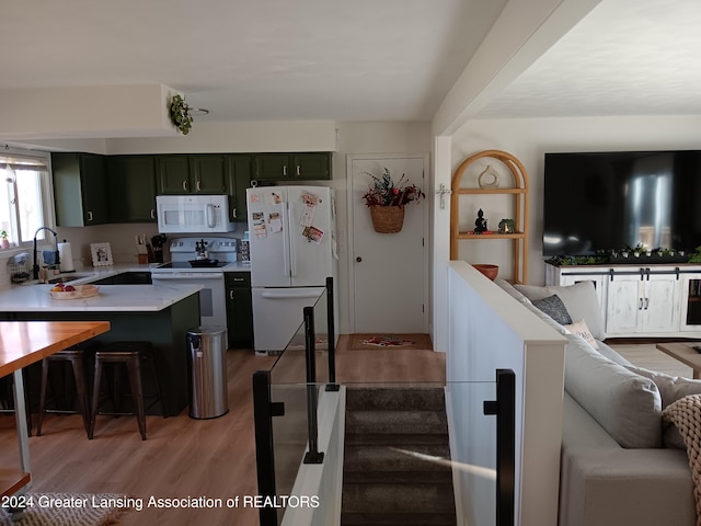 kitchen with a breakfast bar, white appliances, sink, light hardwood / wood-style flooring, and green cabinetry