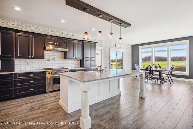 kitchen featuring light stone countertops, stainless steel range, a breakfast bar, dark hardwood / wood-style floors, and an island with sink