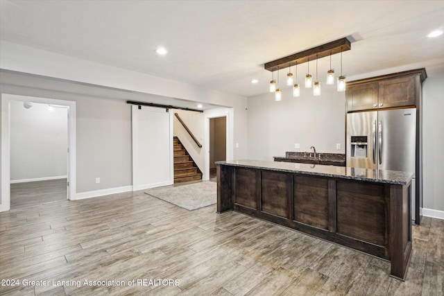 kitchen featuring a barn door, light hardwood / wood-style flooring, dark stone counters, and decorative light fixtures