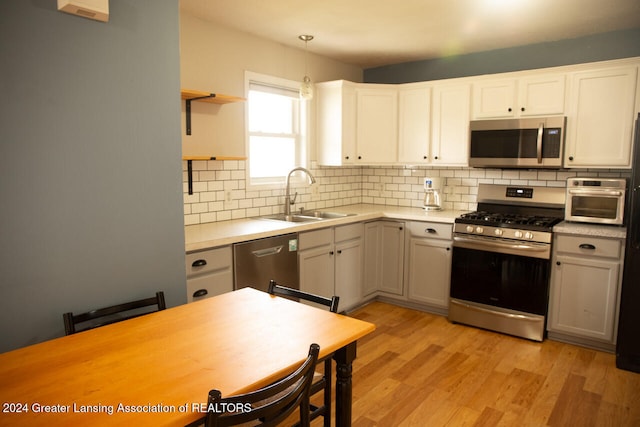 kitchen with sink, light hardwood / wood-style flooring, tasteful backsplash, decorative light fixtures, and stainless steel appliances