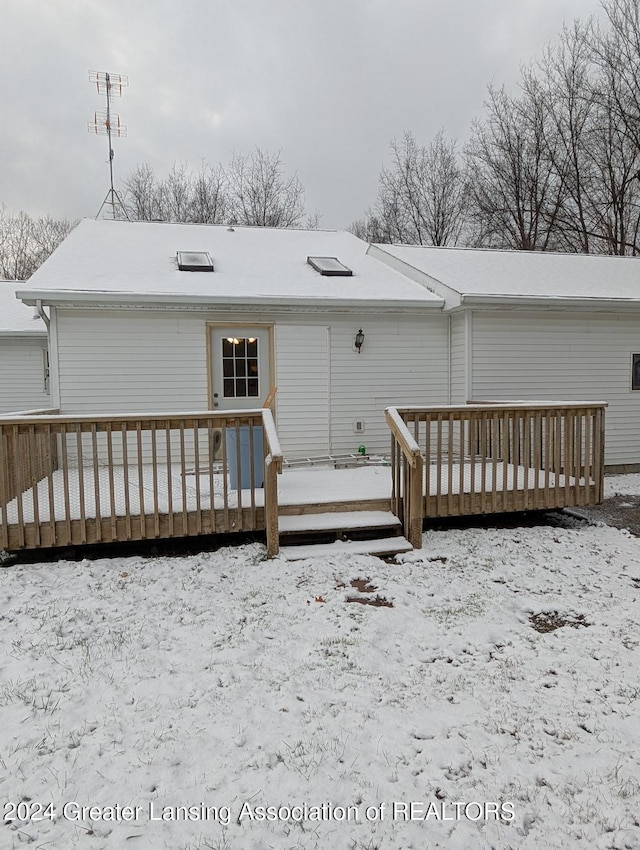 snow covered back of property with a wooden deck