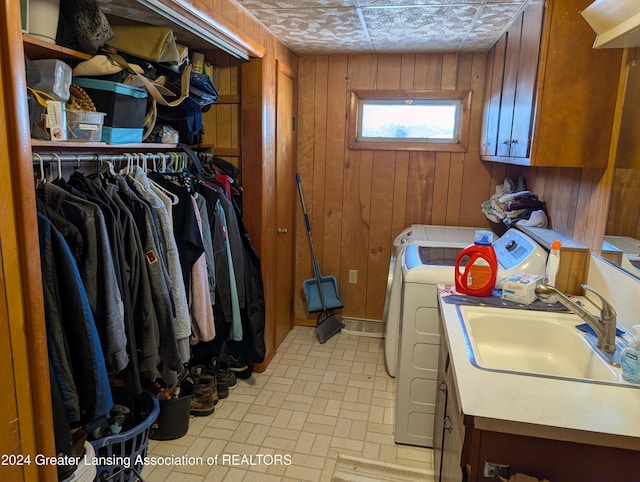 washroom with cabinets, washing machine and dryer, wooden walls, and sink