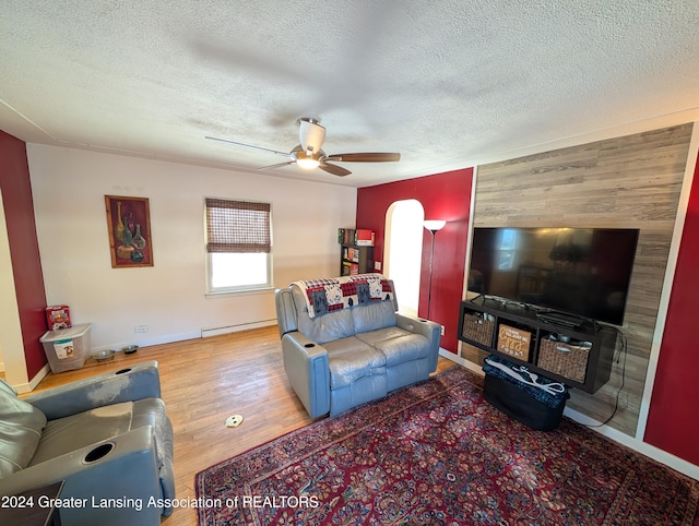 living room with ceiling fan, baseboard heating, hardwood / wood-style floors, a textured ceiling, and wooden walls