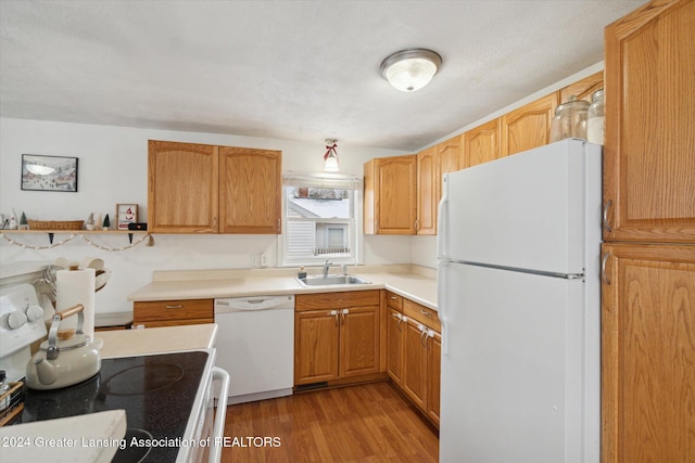 kitchen featuring a textured ceiling, sink, light hardwood / wood-style floors, and white appliances