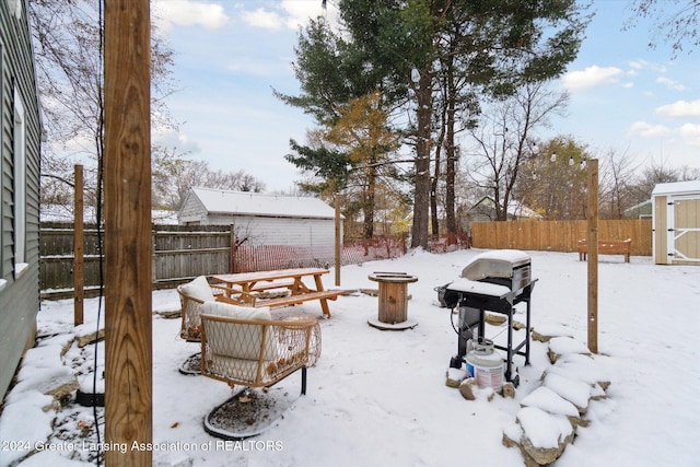 yard covered in snow with a storage shed and an outdoor fire pit