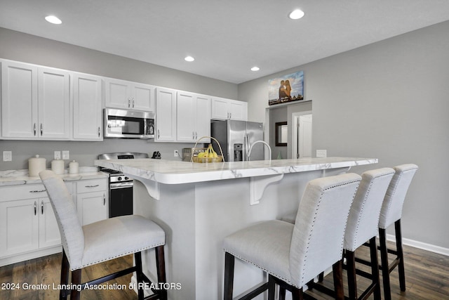 kitchen with appliances with stainless steel finishes, a kitchen island with sink, white cabinetry, a kitchen bar, and dark wood-style floors