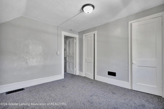 unfurnished bedroom featuring carpet flooring, a textured ceiling, and vaulted ceiling