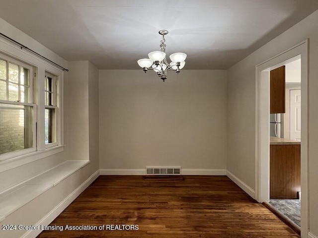 unfurnished dining area with a notable chandelier and dark wood-type flooring