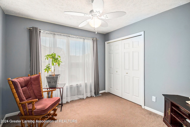 sitting room with ceiling fan, light colored carpet, and a textured ceiling