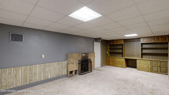 unfurnished living room with wooden walls, a drop ceiling, and carpet