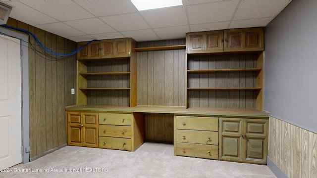 unfurnished office featuring light colored carpet, a drop ceiling, and wood walls