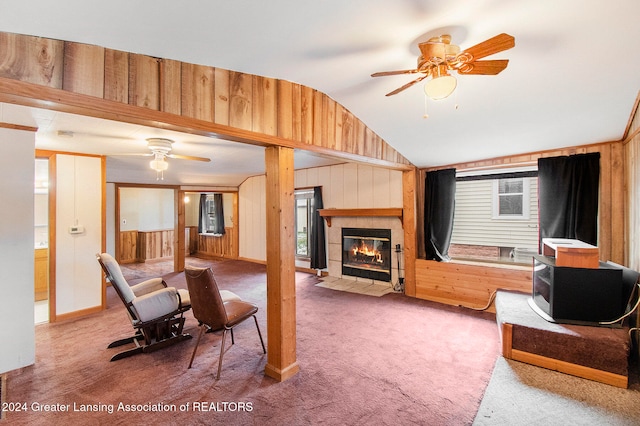 living room with carpet, lofted ceiling, wooden walls, ceiling fan, and a tiled fireplace