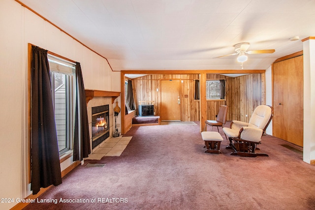 living area featuring a fireplace, light carpet, wooden walls, and ceiling fan