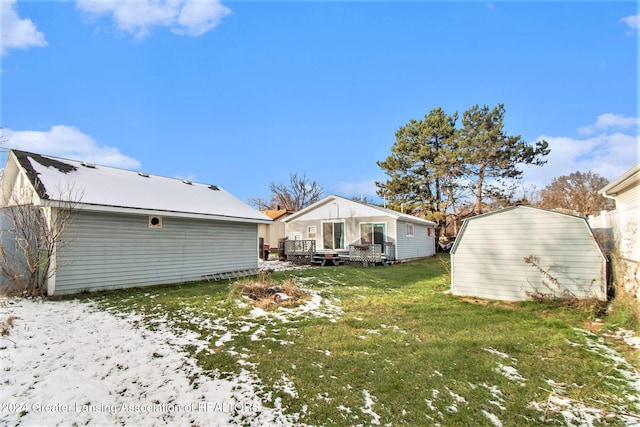 snow covered back of property featuring a lawn, an outbuilding, and a deck