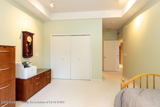 bedroom featuring rail lighting, a tray ceiling, a closet, and light colored carpet