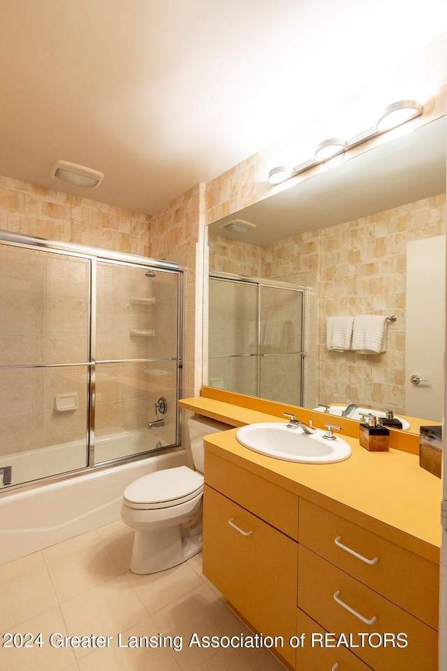 full bathroom with vanity, shower / bath combination with glass door, tile patterned flooring, toilet, and tile walls