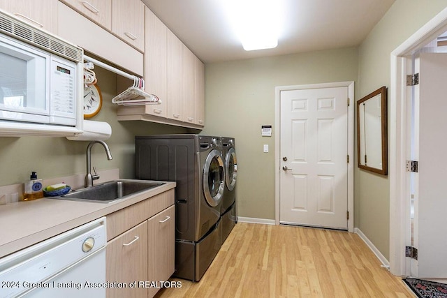 clothes washing area featuring washer and dryer, sink, cabinets, and light hardwood / wood-style floors