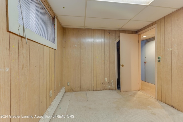 carpeted spare room featuring a paneled ceiling and wooden walls