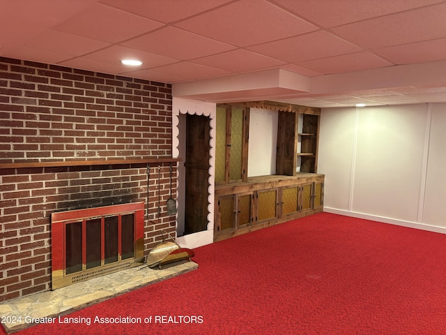 basement featuring carpet floors, a brick fireplace, and a paneled ceiling